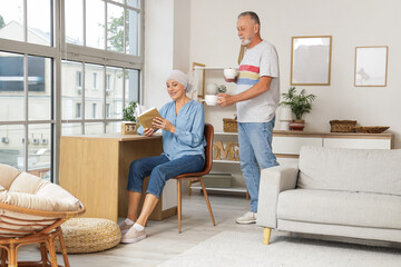 Sticker - Mature woman after chemotherapy with book receiving cup of tea from her husband at home