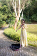 © Masakazu Tokashiki - Young Chinese Malaysian woman in her 20s playing violin near a fountain pond in a large park in Bukit Jalik, Malaysia, wearing a yellow dress.