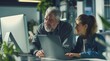 © yj - Professional mature business man and young woman leader, two colleagues talking working on computer at work desk.