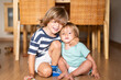 © Nanci - Affectionate siblings, a boy and baby, hugging and sitting on the wooden floor.Cute brother and sister embracing and smiling on the floor.