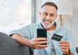© K Davis/peopleimages.com - Relax, mobile and mature man with credit card on sofa for transaction, e commerce or online shopping in living room. Payment, app and person for purchase, subscription or internet banking in home