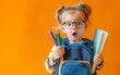 © Viktoriia - Enthusiastic young girl with pigtails and glasses, holding colored pencils and notebooks, expressing surprise on bright orange background, ready for school