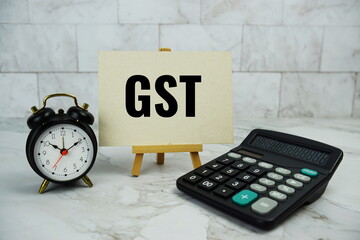 GST, goods and services tax text written on paper card with calculator and alarm clock on marble background