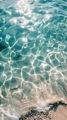 Wall Mural - sea water waves texture ripples on water surface light blue ocean water top view clear aqua background sun glow reflection white sand bottom stones underwater tropical island beach