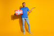 © deagreez - Full length photo of handsome young guy hold gift skeptical empty space dressed stylish blue garment isolated on yellow color background