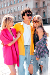 Group of young three stylish friends posing in the street. Fashion man and two cute female dressed in casual summer clothes. Smiling models having fun in sunglasses. Cheerful women and guy outdoors