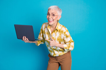 Wall Mural - Photo portrait of attractive senior woman hold point excited netbook dressed stylish elegant clothes isolated on blue color background