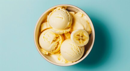 Canvas Print - Bowl of banana yellow ice cream scoops on light blue background, top view, minimal flat lay style.