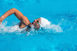 © Microgen - Female swimmer in white swim cap and goggles performing freestyle stroke in an outdoor pool, highlighting competitive swimming, athletic performance, and training