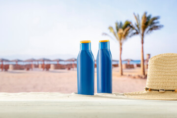 Wall Mural - Blue containers for sun tan lotion and sunscreen oils on a bright table with tropical  beach and a sea and clear sky background.