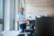 © Westend61 - Smiling businessman standing with tablet PC and looking through window in office