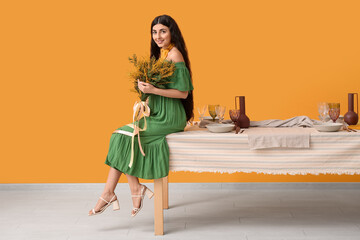 Beautiful young woman with bouquet of mimosa flowers in dining room