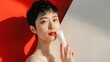 © WITTAYA  ANGMUJCHA - Short-haired Chinese girl holds skin care products on your face. red and white background