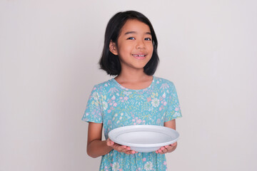 Wall Mural - Little girl smiling at the camera while holding an empty dining plate