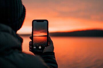 A person is holding a cell phone up to their eye, taking a picture of the sunset