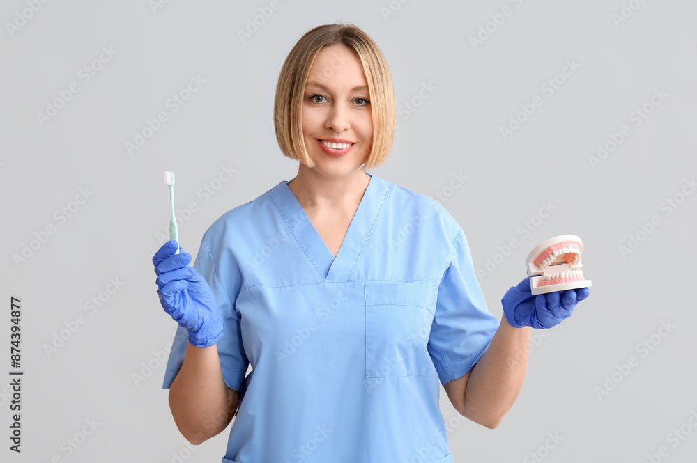 Female dentist with tooth brush and plastic jaw on grey background