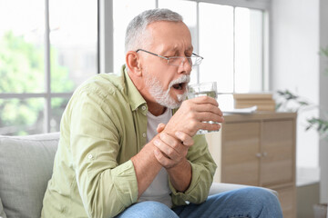 Wall Mural - Senior man suffering from Parkinson syndrome drinking water at home