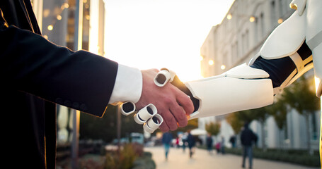 Shaking hand with artificial intelligence machine. Businessman shakes iron robot's hand. Agreement on business future.