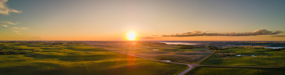 Wall Mural - A wide aerial panoramic view of the sun setting over a vast prairie agricultural landscape that is cut by gravel roads.  The setting sun highlights the rolling farm fields.
