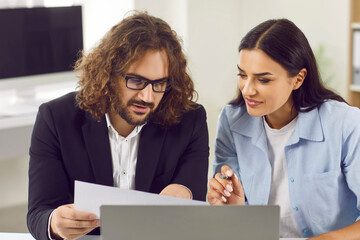 Two concentrated serious business people and company employees work in office sitting at the desk with laptop and looking through financial documents on workplace. Accountant job concept.