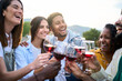 © CarlosBarquero - Cheerful group of multiracial friends toasting glasses of red wine together laughing at terrace house outdoors. Cheers of smiling diverse millennial community people having fun at sunset summer party