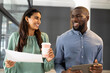 © Wavebreak Media - Holding coffee cup and documents, woman talking with man holding tablet in office