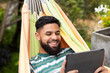 © Wavebreak Media - Using tablet and smiling, man relaxing in hammock outdoors