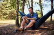 © baranq - Happy adult man using phone sitting in hammock