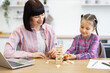 © sofiko14 - Mother and daughter enjoying quality time playing block game at home. Woman in casual clothing with girl building tower of wooden blocks. Concepts of family bonding and childhood development.