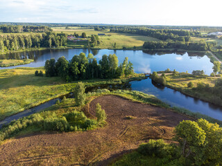 Wall Mural - A beautiful summer landscape of a small lake, green trees and fields, taken from a drone. Natural rural landscape of Latvia, Northern Europe.