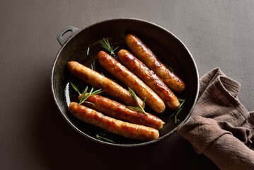 Wall Mural - Delicious thin sausages in frying pan on dark background