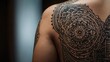 © Adam - Close-up of an intricate mandala tattoo on a person's shoulder, showcasing detailed patterns and artistic design.