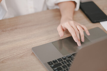 A woman is using a laptop on a wooden table. She is touching the screen with her finger