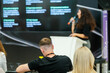 © Anton Gvozdikov - Female speaker giving a presentation at a professional business conference. Audience members are attentively listening and taking notes.