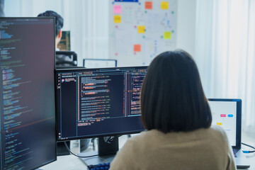 Wall Mural - Asian software developers working on multiple screens displaying code and application diagrams in a modern office