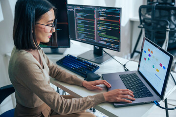 Asian prompt engineer develop coding app with software data sitting in front of computer monitor at office