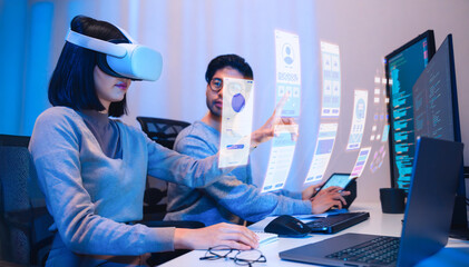 Wall Mural - asian software developer wearing a virtual reality headset works on a vr project, with a colleague f