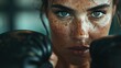 © familymedia - A close-up image of a person wearing black boxing gloves, staring with intense focus and determination, showcasing their freckle-covered face and strong will in a gym setting.