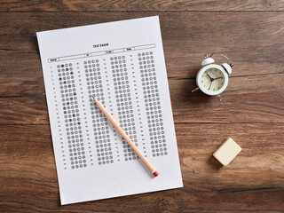 Wall Mural - Top view of a test exam paper with alarm clock, pencil and an eraser on a wooden school desk.