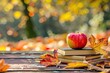 © Tin - Apple on books with autumn leaves on a wooden table. Warm fall colors in the background. Perfect for education and seasonal themes.