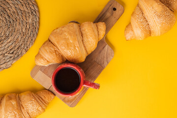 Wall Mural - Flat lay of freshly baked croissants on the yellow background. Traditional French pastry with a cup of black coffee. Copy space for a free text