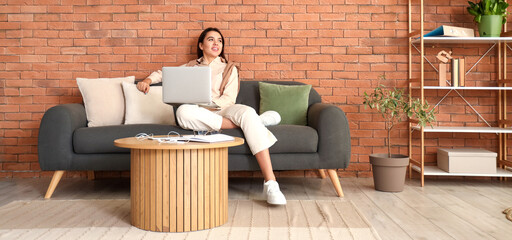 Sticker - Young woman working with laptop on sofa at home office