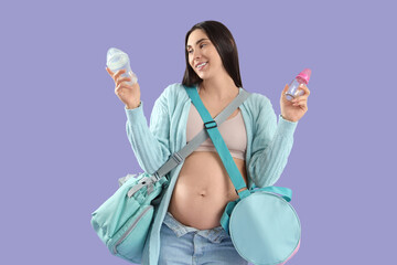 Canvas Print - Young pregnant woman with maternity hospital bags and baby bottles on lilac background