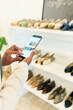 © peopleimages.com - Woman, hand and shoe store with smartphone, picture and retail product in business with professional buyer. Sourcing supplier, email and image of stock for new range, ladies footwear and shopping