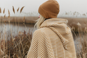 Wall Mural - A woman wearing a brown hat and a yellow and white blanket stands in a field