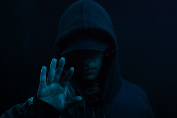 Mysterious young man in a sweatshirt showing his palm to the camera. Face hidden. Studio portrait.