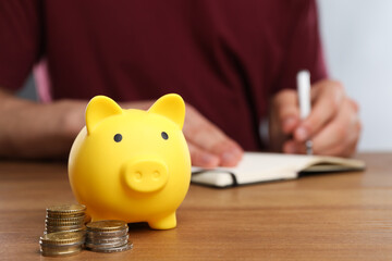 Poster - Man at wooden table, focus on yellow piggy bank and coins. Space for text