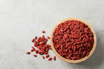 Wall Mural - Dried goji berries in bowl on light textured table, top view. Space for text