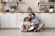 © fizkes - Happy family with little daughter sit on warm floor with underfloor heat system in modern home kitchen, enjoy time together, playtime and their good harmonic relations at new own or rented apartment