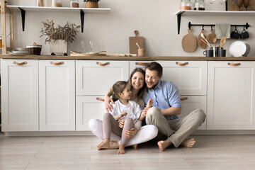 Happy family with little daughter sit on warm floor with underfloor heat system in modern home kitchen, enjoy time together, playtime and their good harmonic relations at new own or rented apartment